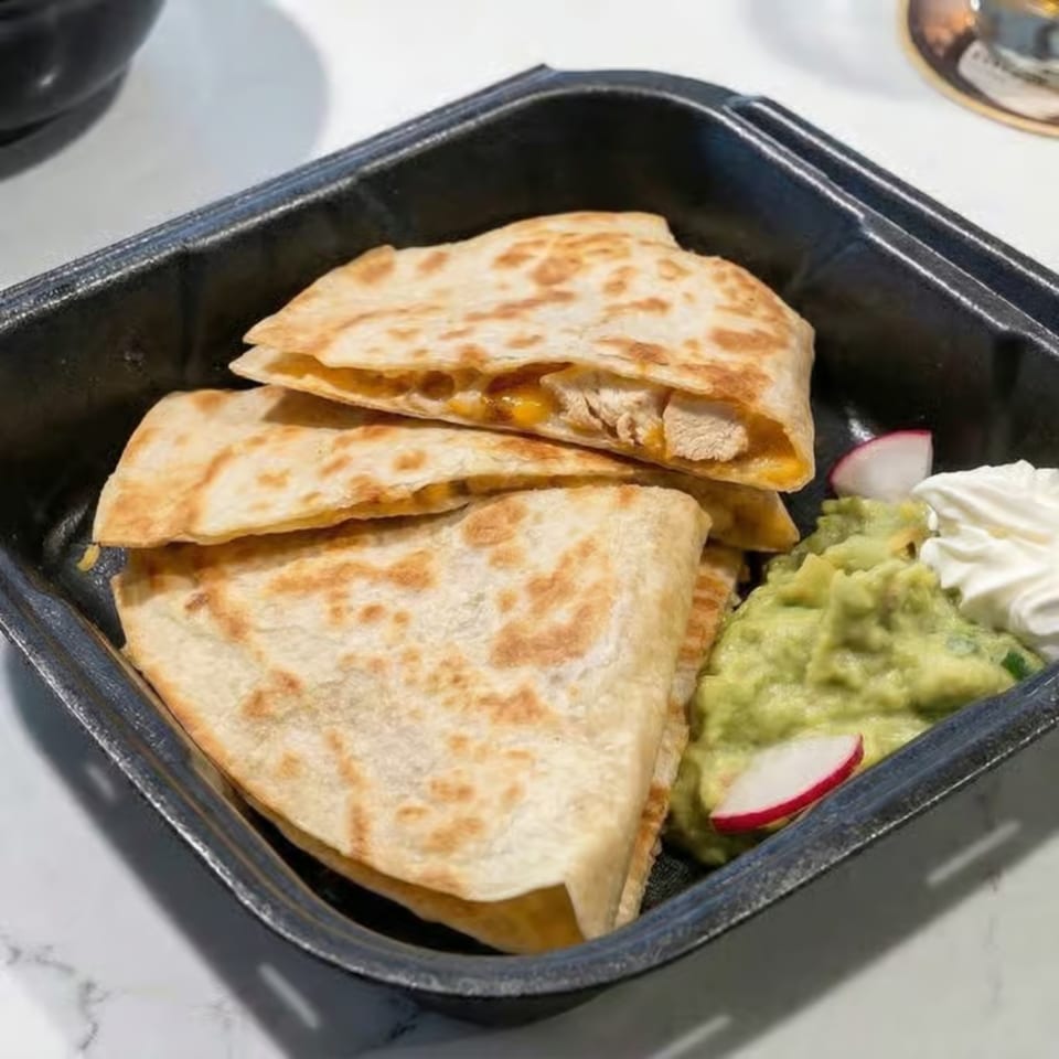 Chicken quesadillas with guacamole, sour cream, and radish slices in a black takeout container.